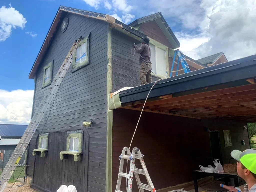Painter cutting in trim on a dark-stained two-storey exterior