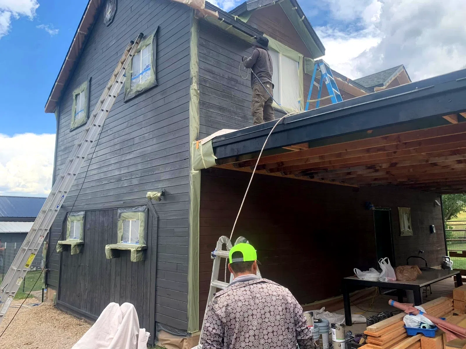 Painter on a ladder applying fresh exterior paint to a two-story home
