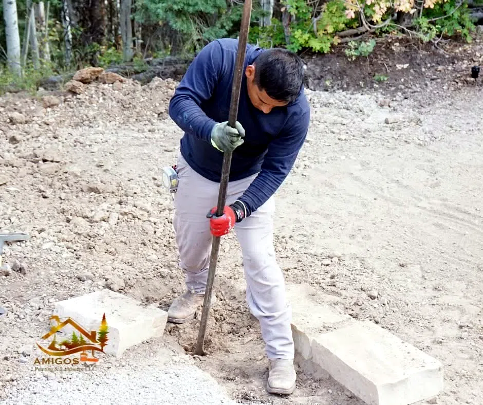Crew member breaking ground with a digging bar beside new paver edging