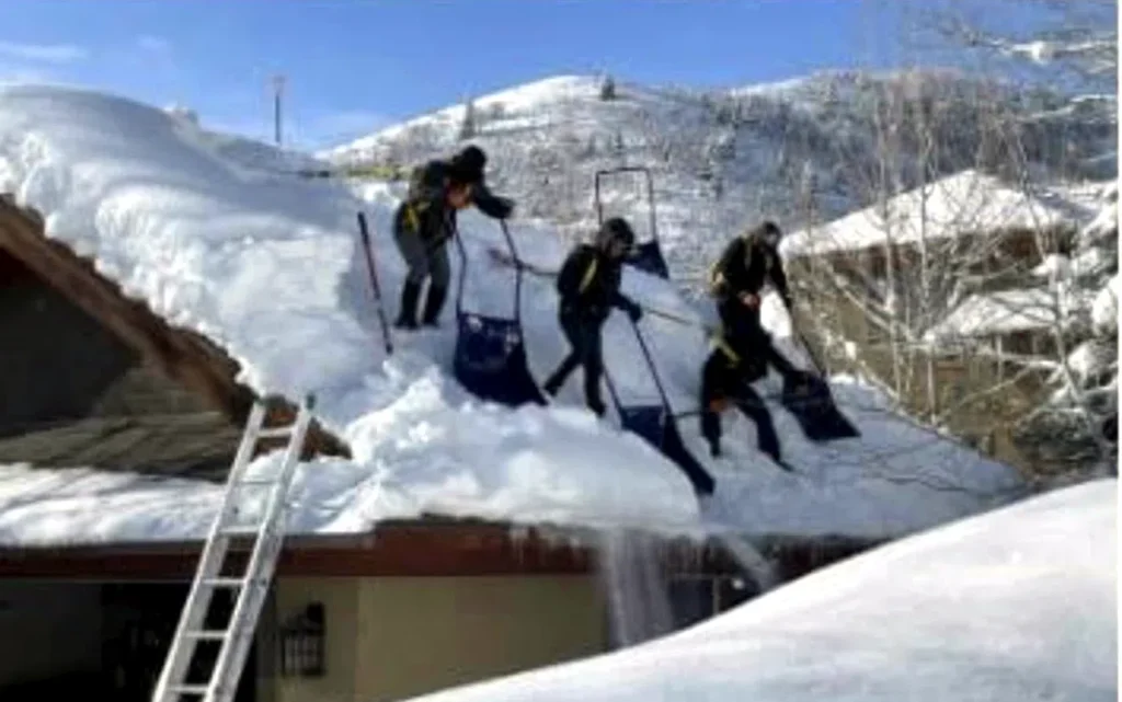 Three crew members shovelling a snow-loaded roofline