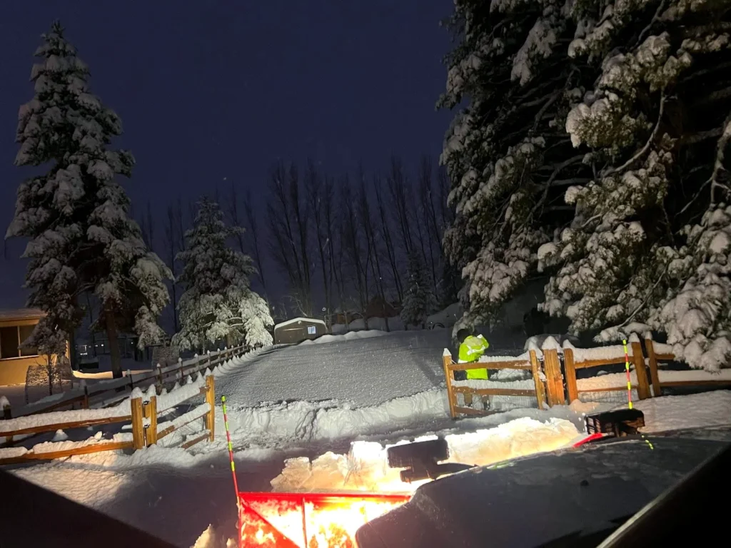 Night-time snow clearing lit by work lights at a Heber Valley property